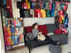 a woman sitting on top of a couch in front of a wall full of yarn