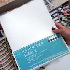 a person holding up a white sheet of paper in front of some crafting supplies