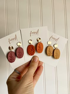 three pairs of earrings are shown in front of a white wall and one is holding the other