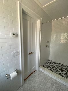 a bathroom with white tile and black and white tiling on the shower wall, toilet paper roll holder, and tiled floor