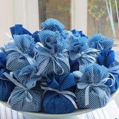 a bowl filled with blue and white fabric balls on top of a table next to a window