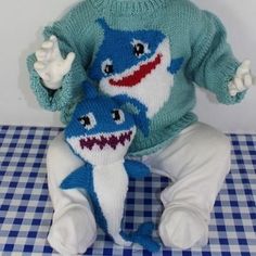 two knitted baby shark dolls sitting on a checkered tablecloth