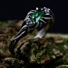 a close up view of a ring with an emerald stone in the center on some rocks