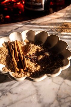 cinnamon sticks and spices in a white bowl on a marble counter top next to a bottle of booze