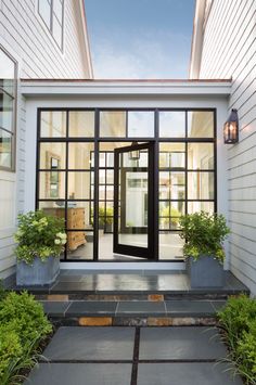 an entry way leading to a house with glass doors and potted plants on the steps