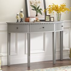 a silver console table with flowers and pictures on the top, in front of a white wall