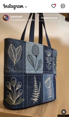 a blue bag with white flowers and leaves painted on it's sides, sitting on top of a wooden table