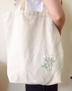 a woman is holding a white bag with daisies embroidered on the front and side