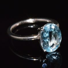 an oval blue topaz ring on a reflective surface with reflection in the dark background