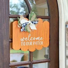 a welcome to our path sign hanging on the front door with pumpkins and gingham