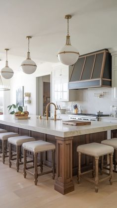 a large kitchen island with four stools in front of it and lights hanging from the ceiling