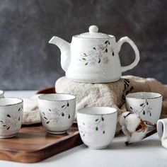 a white tea set sitting on top of a wooden tray next to other cups and saucers