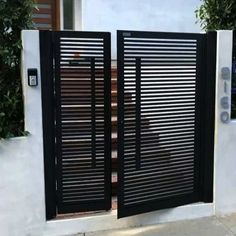 an open gate with black slats on the side of a white wall next to a planter