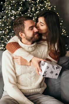 a man and woman kissing while sitting on a couch with a christmas tree in the background