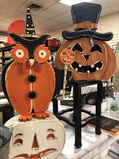 two wooden carved pumpkins with faces and hats on display in a storeroom, one is wearing a top hat