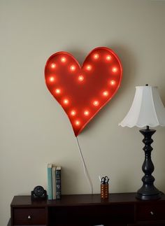 a red heart shaped neon sign sitting on top of a wooden table next to a lamp