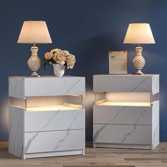 two white marble nightstands with lamps on top and flowers in vase next to them