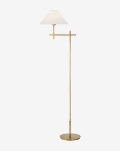 a gold floor lamp with a white shade on the top and a light bulb at the base