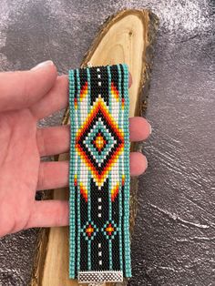 a hand holding a beaded bracelet on top of a piece of wood