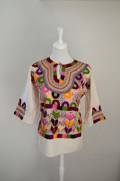 A beautiful hand embroidered blouse made in Chiapas, ideal for spring and summer, simply to be enjoyed. This style of embroidery is called "Milpita" which shows corn leaves in different colors, and sometimes figures of farmers working on the field, just look carefully at the details. Please bear in mind that these pieces are all hand made so sometimes you will find some little flaws, but is all part of the charm. RECOMMENDED FIT: M MEASUREMENTS: Width (armpit to armpit) : 56 cm Length : 64 cm MA Traditional Multicolor Cotton Embroidered Top, Folk Style Multicolor Top With Geometric Embroidery, Folk Blouse With Multicolor Embroidery Motif, Bohemian Embroidered Cotton Top, Bohemian Cotton Embroidered Top, Multicolor Embroidered Cotton Blouse, Traditional Multicolor Blouse With Geometric Embroidery, Multicolor Embroidered Cotton Top For Festivals, Multicolor Cotton Embroidered Top For Festivals