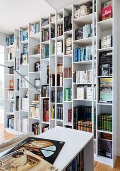 a bookshelf filled with lots of books next to a white table in front of a window