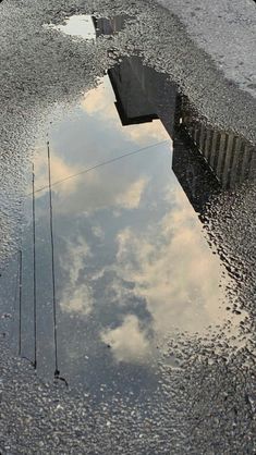 there is a reflection of clouds in the wet pavement and water on the ground,