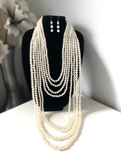 "Layered long white faux pearl necklace set for women Don't miss this opportunity to own this beautiful pearl necklace. This classic necklace is a timeless treasure and add a gorgeous glow to any outfit. Eight layers of pearls make this necklace truly statement piece! This multi strand necklace is made from high quality acrylic pearls, silver lobster clasp and adjustable chain. Measurement: First strands  25\"long+ext.(63 cm) Last strands 48\" long (122 cm) **I will pair this necklace with earri Pearl White Multi-strand Pearl Necklace, Multi-strand Pearl White Necklace With Pearl Pendant, Elegant White Pearl Layered Necklace, Layered Pearl Drop Necklace, Formal Long Pearl Necklace, Pearl Backdrop Necklace For Parties, Party Pearl Backdrop Necklace, White Multi-strand Pearl Necklace For Formal Occasions, Long Pearl Necklace For Party