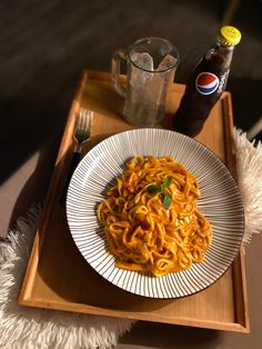 a white plate topped with pasta on top of a wooden tray next to a bottle of soda