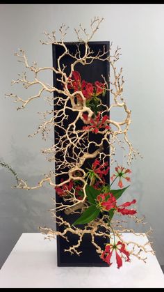 a tall black vase with red flowers and branches in front of a white table top