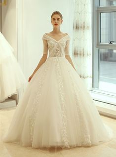 a woman in a white wedding dress standing next to a window