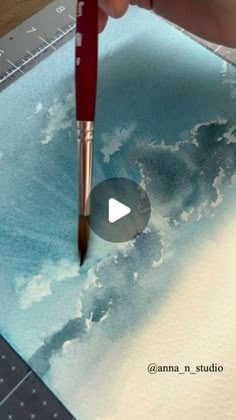 someone is painting clouds on paper with a brush