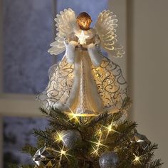 an angel figurine sitting on top of a christmas tree with lights around it