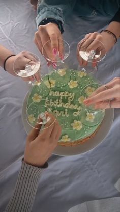 four people are holding wine glasses and reaching for a cake with the words happy birthday written on it