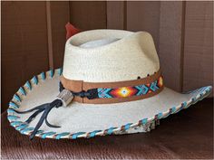 The Nelle starts with a Mexican soft palm leaf hat body that has a 3 3/4" brim and 5 1/4" crown. Hand laced in saddle and turquoise leather lace. The beaded hatband has colors of turquoise and orange and is mounted on tan suede. The back of the band has a deer antler bead for accent. Copper patina Concho and an orange decorative feather completes the hat. Note: Please allow 3-4 weeks. Western Hat Bands With Flat Crown For Beach, Southwestern Turquoise Hat Bands For Country Events, Southwestern Turquoise Hat Band For Ranch, Blue Bohemian Hat Bands, Southwestern Turquoise Hat For Ranch, Southwestern Straw Hat With Flat Brim For Western-themed Events, Western Natural Hat Bands For Festivals, Southwestern Flat Brim Hat Bands For Vacation, Natural Western Hat Bands For Festival