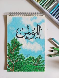 a notebook with an arabic writing on it next to crayons and colored pencils