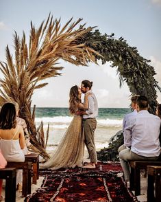 a man and woman kissing in front of an arch with palm trees on the beach