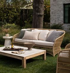 a couch and coffee table sitting in the grass near a tree with pillows on it