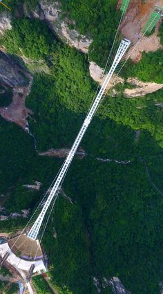 an aerial view of a suspension bridge in the middle of a green mountain range, with trees on both sides