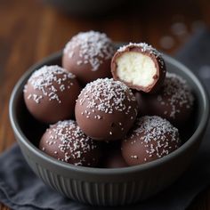 a bowl filled with chocolate covered desserts on top of a wooden table next to a black napkin