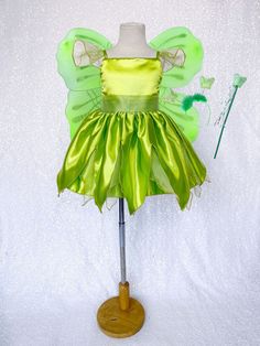 a green fairy dress on a mannequin stand with a white wall in the background