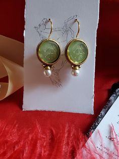 I saw these earrings and knew they were perfect to offer in the shop.  They are gold plated earwires with a round glass green intaglio and pearl drop.  Perfect to wear for late 18th century, early 19th century on up to today.  I love them! They measure 1-1/4 inches long by 3/4 inch wide.  The earwire is super long which is good to stay in the ear. Lots of inspiration on my Pinterest page.  https://www.pinterest.com/kkwalte/_saved/ Yellow Gold Round Earrings With Intaglio, Yellow Gold Round Intaglio Earrings, Round Intaglio Earrings For Anniversary, Vintage Intaglio Earrings For Wedding, Intaglio Drop Earrings For Gift, Victorian Style Pierced Brass Earrings, Victorian Intaglio Earrings For Wedding, Oval Brass Earrings For Formal Occasions, Oval Intaglio Earrings As A Gift