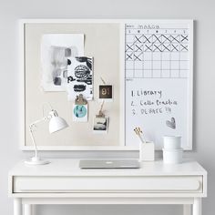 a white desk topped with a laptop computer next to a wall mounted calendar and other items