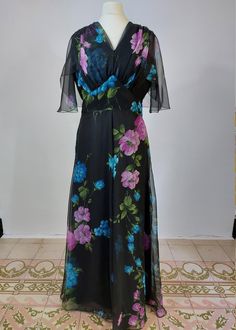 A super example of a perfect summer wedding maxi dress. For those of you who don't like to wear colour but can't wear black to a wedding, this is ideal because the floral design pops! the dress has a ruched v neck and an angel sleeve capelet perfect for keeping upper arms hidden. it has a round back and fastens at the back with a zipper. MEASUREMENTS  * All measurements taken flat then doubled - please ensure fit before purchasing BEST FIT: UK 12  /US  8 / EU  40 APPROX!  - please go by measurements below: Bust: 37 ins/ 94cm  Waist : 29 ins/ 74cm  Hips: free Length (shoulder to hem):57ins/ 145cm Condition: Excellent. She has been professionally cleaned and is ready to wear. There are no noticeable holes or stains on the dress please contact me with any questions or if you want additional p Spring Party Maxi Dress With Flutter Sleeves, Summer Party Maxi Dress With Flutter Sleeves, Summer Party Gown With Floral Print, Summer Maxi Length Prom Gown, Summer Prom Gown Maxi Length, Summer Evening V-neck Gown, Black Chiffon Maxi Dress With Floral Print, Summer Chiffon Gown With V-neck, Summer Maxi Evening Dress For Wedding Guest