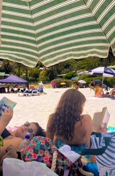 two people are laying on the beach under an umbrella reading books and drinking water from a bottle