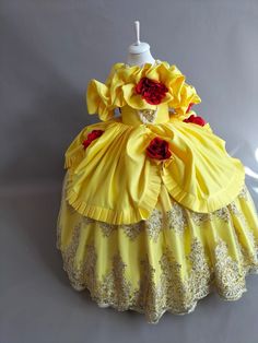 a yellow dress with red flowers on the bottom and lace around the bust, sitting on a white surface