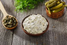 two wooden bowls filled with dip and pickles on top of a table next to other foods