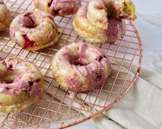 several doughnuts with pink icing sitting on a wire rack