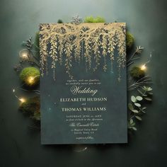 an elegant wedding card with gold foil on it and greenery in the background, surrounded by lights