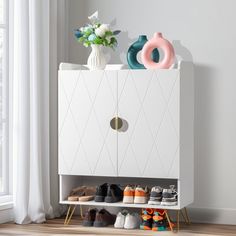 a white cabinet with shoes on it and a vase filled with flowers next to it