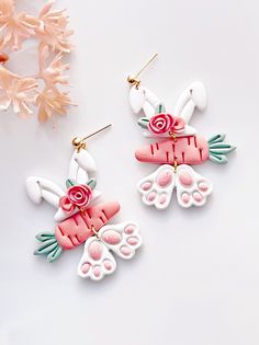 two pairs of pink and white earrings with flowers on them next to a flower arrangement